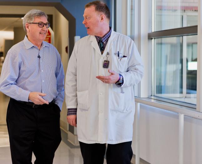 A physician and patient walk and talk down a hospital hallway.