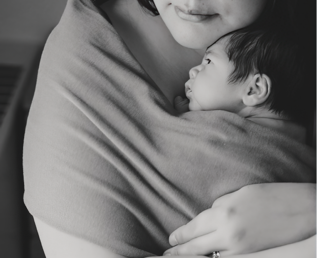 A mother cradles a baby to her chest in swaddling.