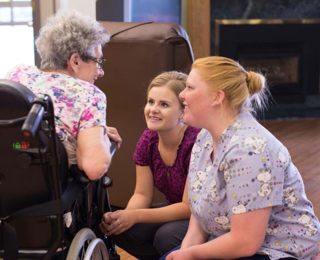 Two health professionals kneeled down to interact closely with a senior resident