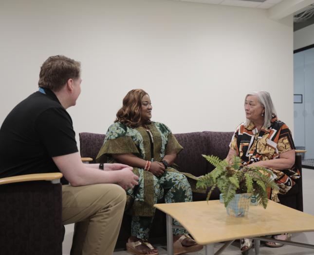 Three people engaged in conversation in a welcoming lounge setting at Covenant Health, with a plant on the table in the foreground.