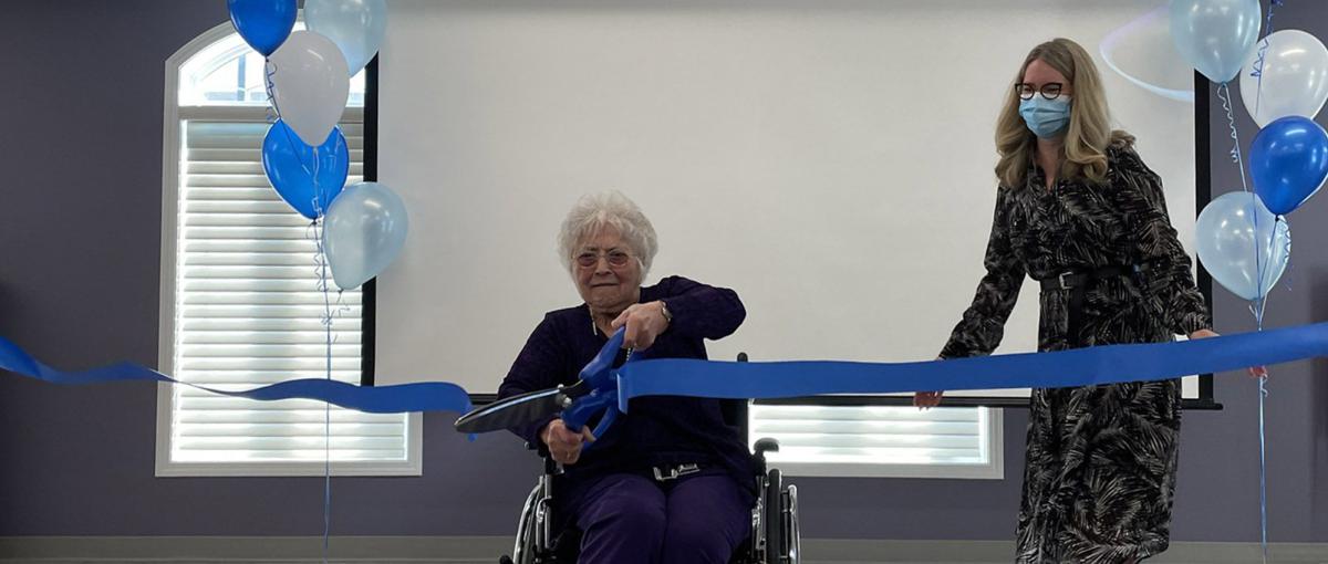 Blanche Gau uses giant scissors to cut a blue ribbon in the redeveloped multipurpose space at Youville Home