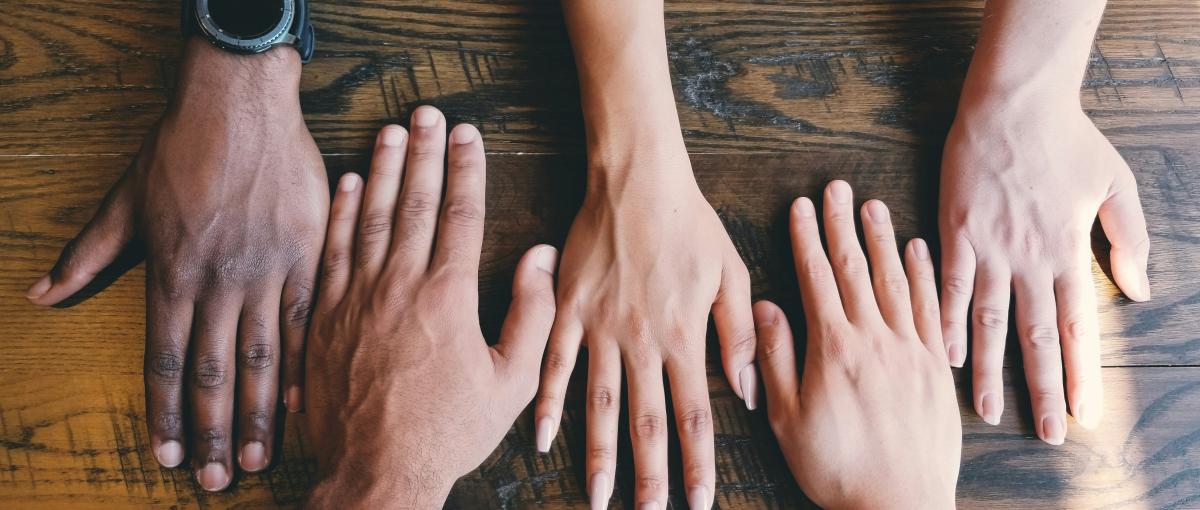 Five hands rest on a wooden surface