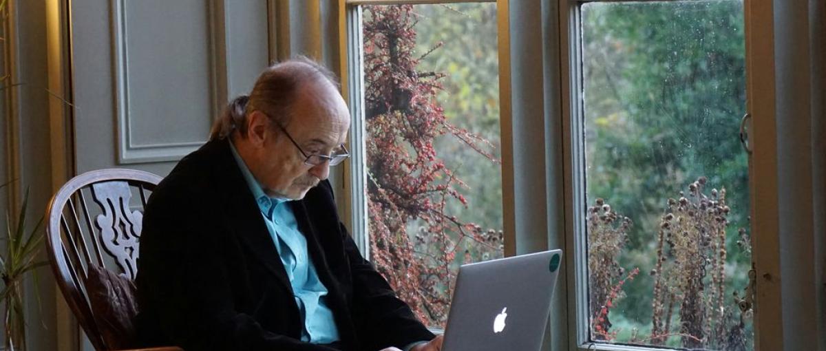 A senior works on a laptop at a dining table.