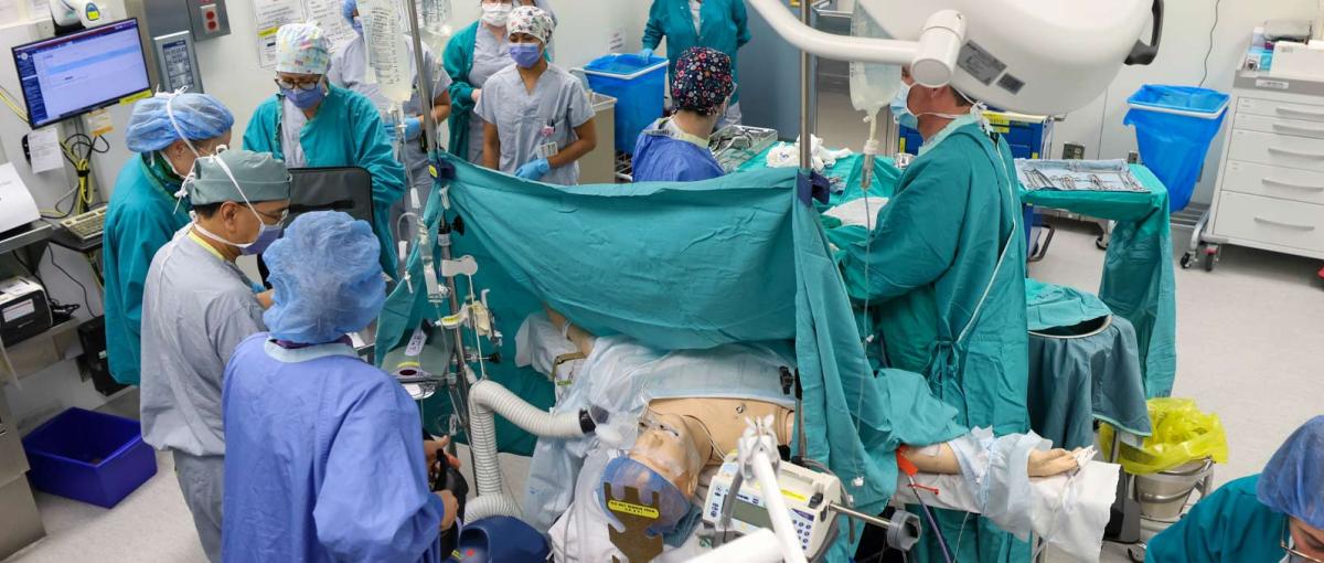 Surgeons in an operating room surround a mannequin during a surgery simulation