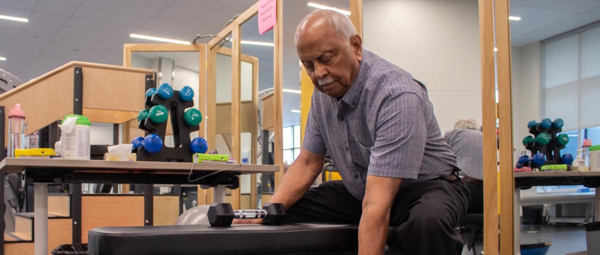 Man exercising with dumbbells while sitting on a bench in a fitness room
