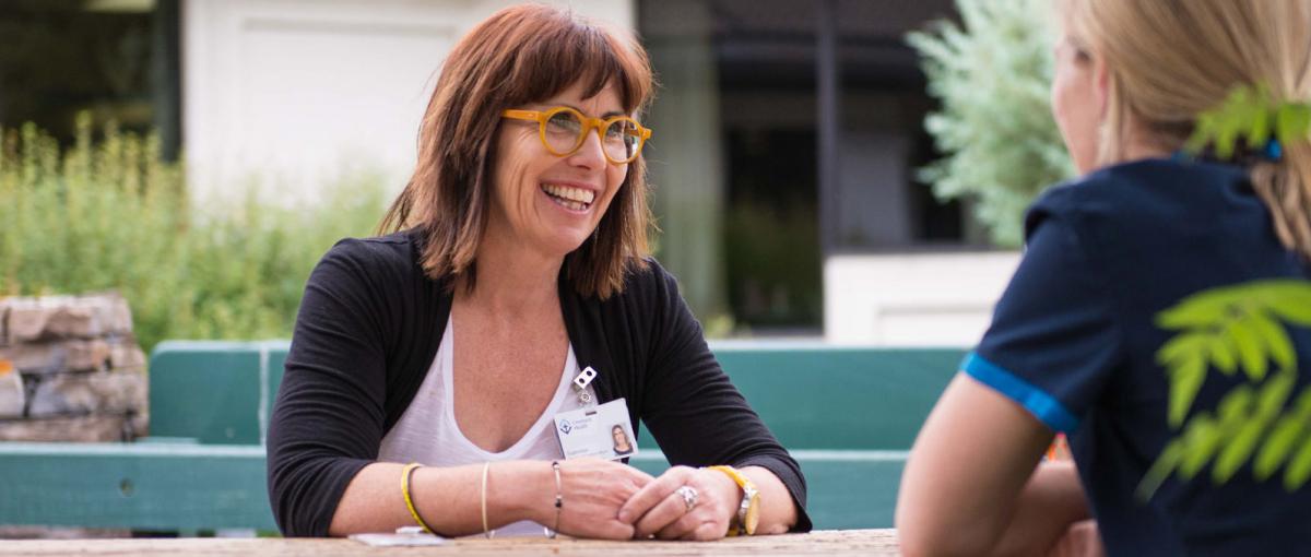 A smiling Covenant Health leader sits with an employee at an outside table