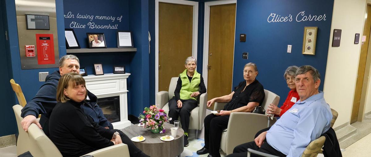 People sitting around a coffee table in front of photos and a dedication to Alice Broomhall
