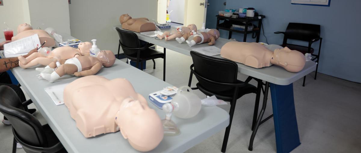 Mannequins with breasts and diverse skin tones are laid out on tables for basic life support training.