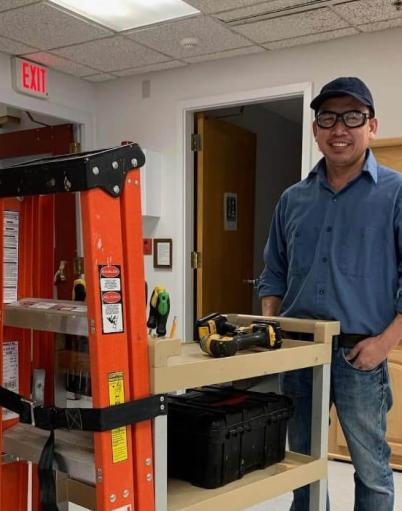 Maintenance worker Generoso Gozo poses by a cart carrying power tools and a ladder