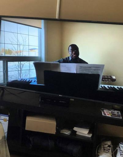 A male senior watches a man on his television who is sitting in front of a piano holding a guitar