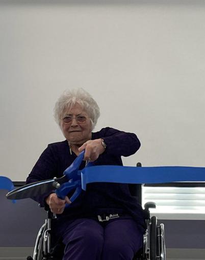Blanche Gau uses giant scissors to cut a blue ribbon in the redeveloped multipurpose space at Youville Home