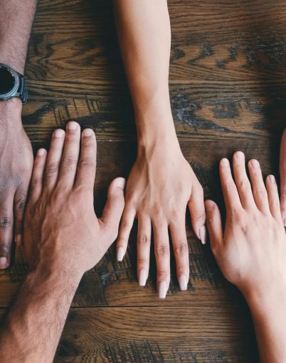 Five hands rest on a wooden surface