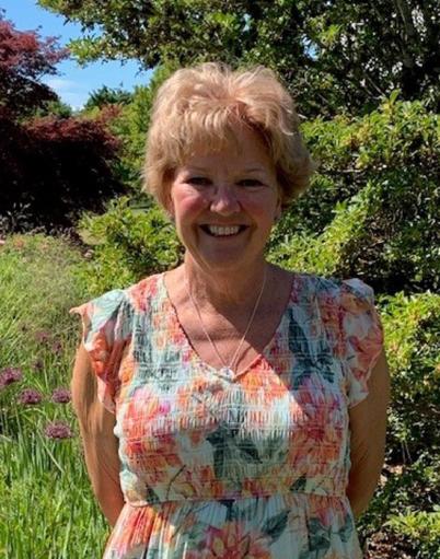 Smiling woman in summer dress poses in front of trees and vegetation