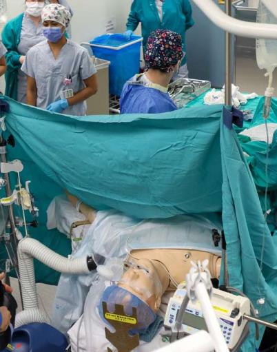Surgeons in an operating room surround a mannequin during a surgery simulation
