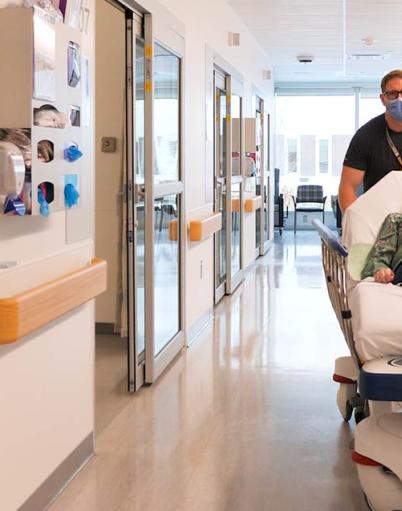 A healthcare worker transports a patient on a gurney down a hospital hallway.