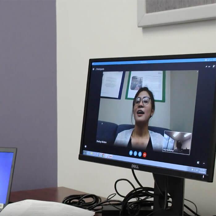 A woman displayed on a computer monitor speaks during a virtual meeting