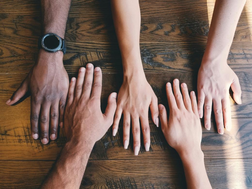 Five hands rest on a wooden surface