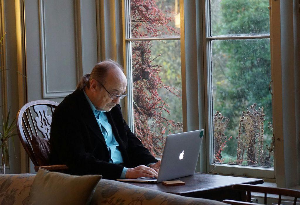 A senior works on a laptop at a dining table.