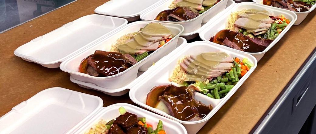 Rows of food trays containing rice turkey with gravy and vegetables on a table