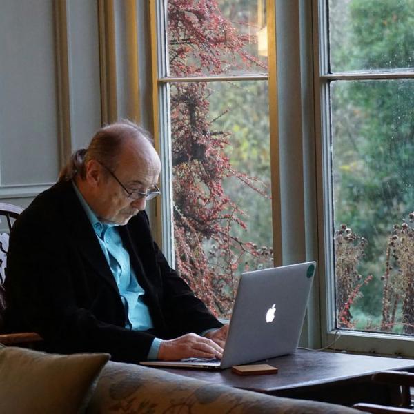 A senior works on a laptop at a dining table.