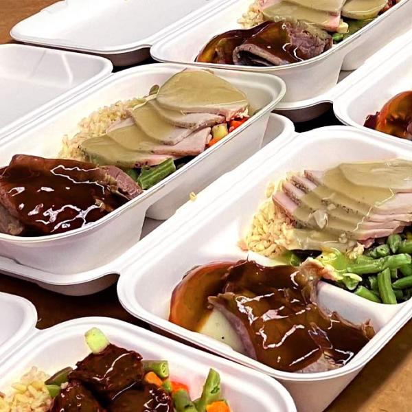 Rows of food trays containing rice turkey with gravy and vegetables on a table