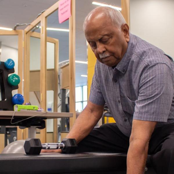 Man exercising with dumbbells while sitting on a bench in a fitness room