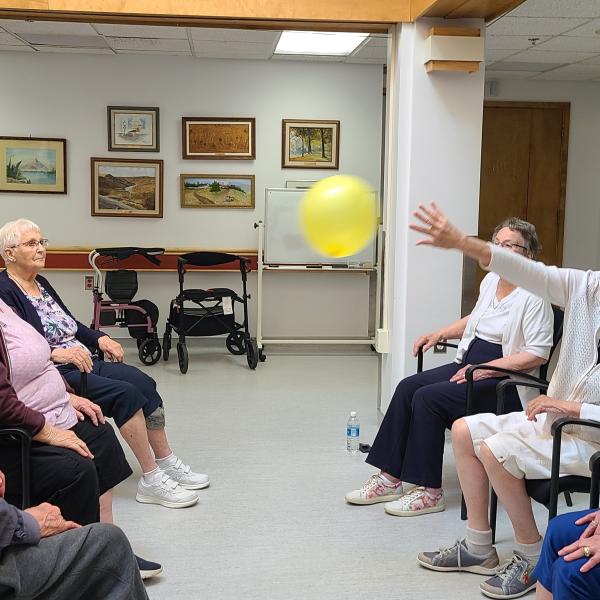 Seniors sitting together while keeping a balloon in the air.