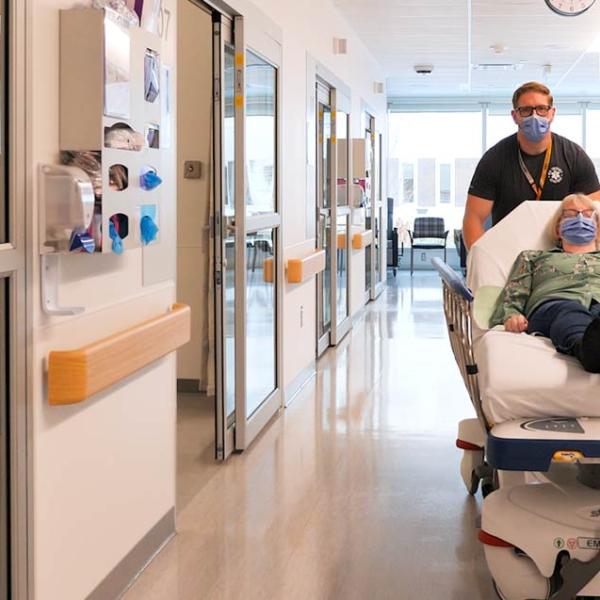 A healthcare worker transports a patient on a gurney down a hospital hallway.