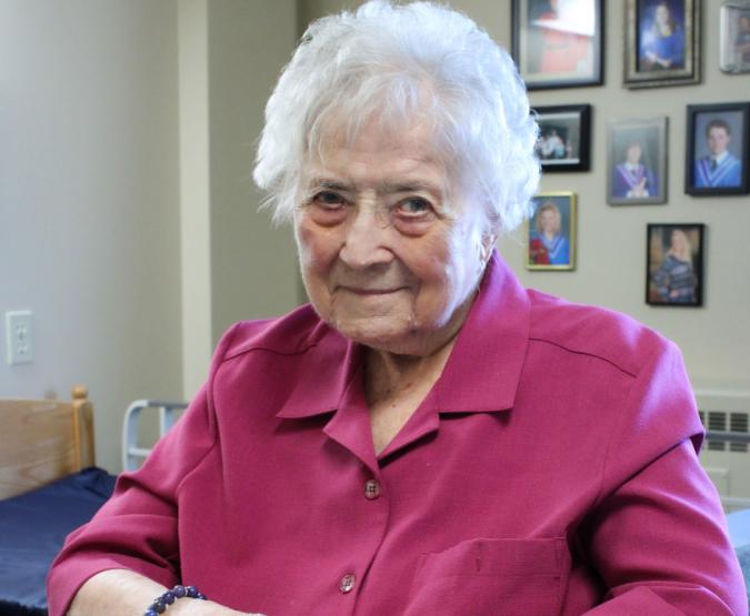 Blanche sits in her room with family photos displayed on the wall behind her