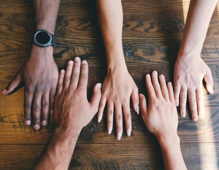 Five hands rest on a wooden surface