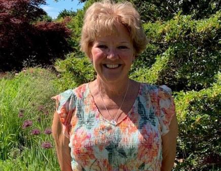 Smiling woman in summer dress poses in front of trees and vegetation