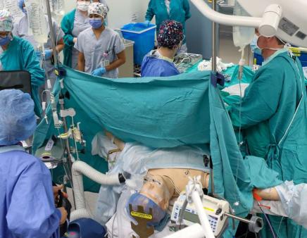 Surgeons in an operating room surround a mannequin during a surgery simulation